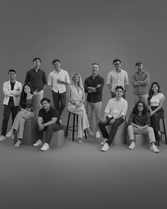 The Goss Group team, twelve people posed on stools and blocks in a grey studio.